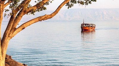 En turistbåt glider fram på en stilla Gennesarets sjö, med Golanhöjderna på andra sidan.